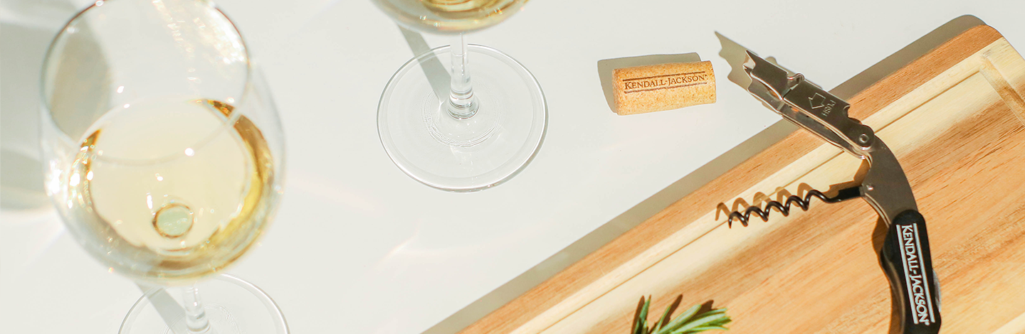 Close up of Kendall-Jackson branded corkscrew, cork and white wine in glasses.